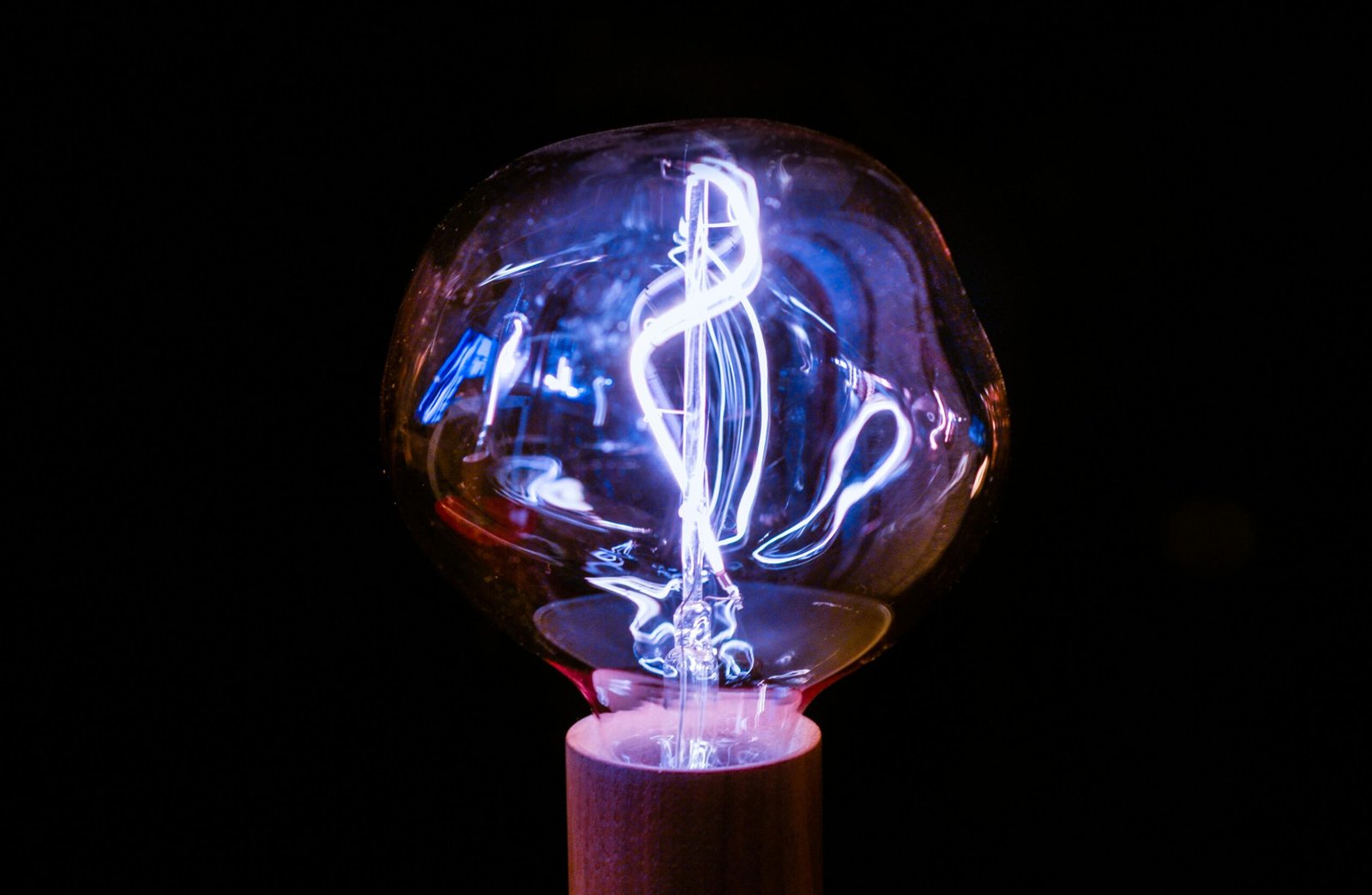 Close-up of a glowing vintage light bulb with an intricate filament design against a dark background.